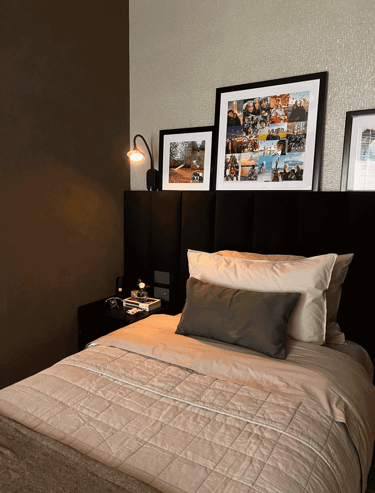 Cama individual con cabecera negra, cuadros y lámpara de lectura encendida | KARÄNA