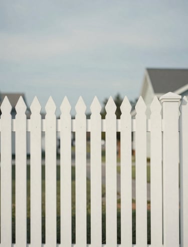 A minimalist view of a white picket fence in a North American suburb under a soft, overcast sky. The composition emphasizes geometric patterns and quiet elegance in off-white and soft blue-grey.