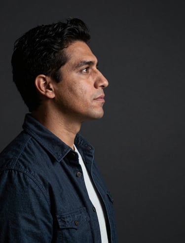 A portrait of an artist in profile, looking at a blank space, in a dark studio. Soft focus, dramatic lighting, contemporary Latinoamericano / Español attire.