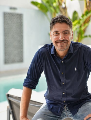 Smiling man in a navy blue Ralph Lauren polo shirt sitting outdoors by a swimming pool.