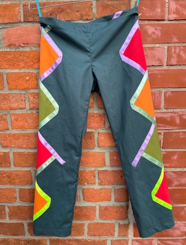 Dark teal pants with colorful geometric patchwork hanging against a rustic red brick wall.
