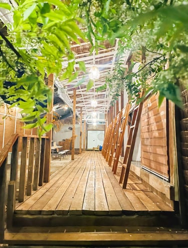 Rustic wooden walkway with hanging pendant lights and lush greenery in a tropical eco-resort.