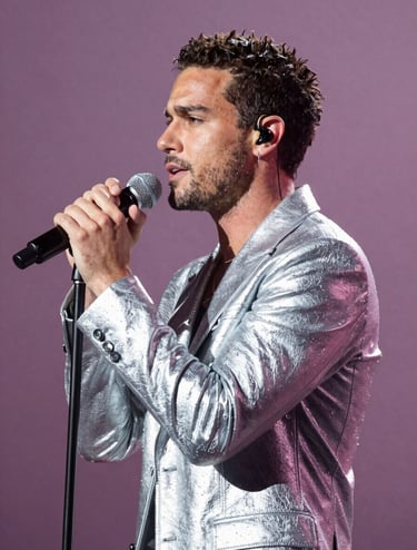 A side-profile photograph of Stefan Taylor performing on stage. He is holding a professional microphone, his expression focused and passionate. The lighting is a dramatic soft silver against a muted plum stage background.