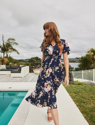 Fashion campaign photography - a woman in a floral dress standing on a patio by a pool