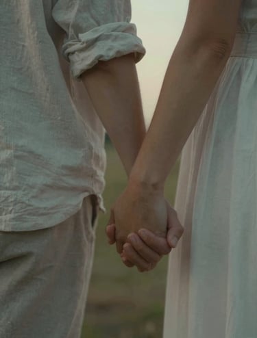 A close-up, cinematic shot of a couple's hands intertwined, wearing soft linen textures in #E2D7C3 tones. The lighting is a warm, hazy golden hour glow with subtle #AD7B5B highlights, capturing a spontaneous and intimate moment.