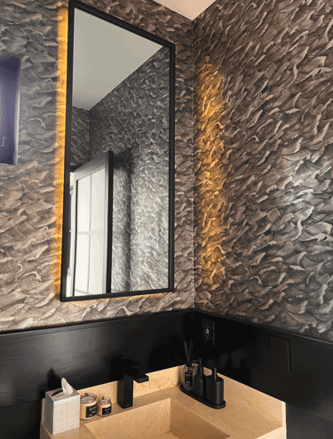 Detalle de baño decorado con papel tapiz texturizado e iluminación cálida indirecta en muro | KARÄNA