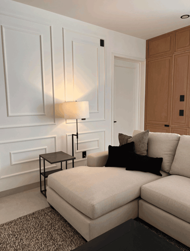 Sala con paneles blancos decorativos, sofá beige tipo chaise lounge y acentos en negro | KARÄNA