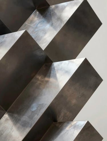 Detail of a geometric metal sculpture with a polished finish reflecting muted gallery tones. Shadows are deep #1A1A1A, highlights are #F9F7F0. Luxurious, modern, and sharp architectural style.
