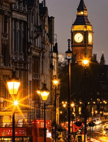 Night view of Big Ben and a red double-decker bus on a glowing London street with streetlights.