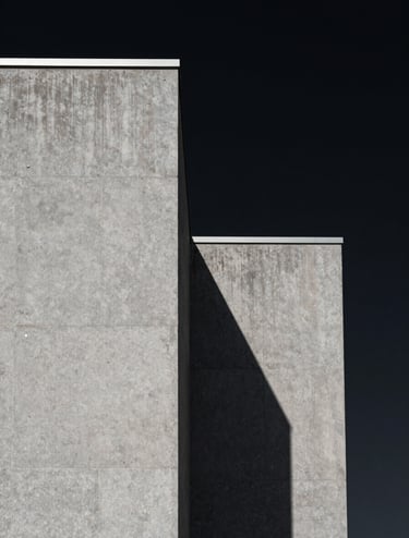 A minimalist architectural detail of a North American building, featuring sharp concrete angles against a deep black sky. The composition is clean and focuses on the texture of the medium gray stone and the dramatic shadow cast by the afternoon sun.