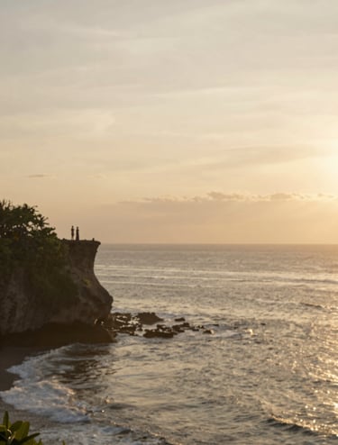 A wide-angle, serene shot of the Bali coastline at golden hour. The sky is a soft blend of #F7F3EE and muted gold. In the distance, the silhouette of a couple stands on a cliff edge, capturing a sense of scale and peace. The lighting is warm and ethereal, reflecting the brand's heartfelt elegance.