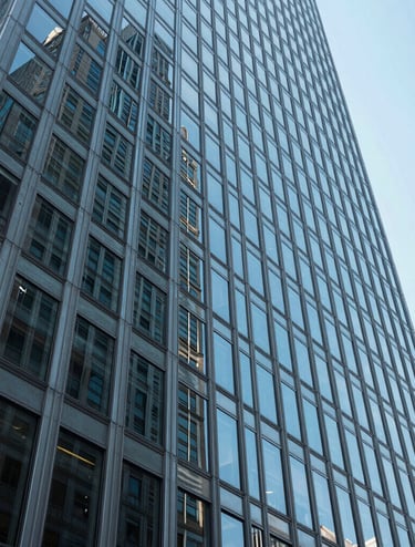 Abstract low-angle shot of a modern glass and steel skyscraper in New York, reflecting a clear light blue sky, emphasizing sharp geometric lines and cutting-edge architectural design.