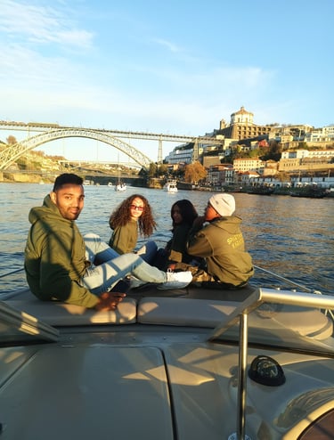 Friends on a boat tour in Porto passing the Dom Luís I Bridge and Douro River at sunset.
