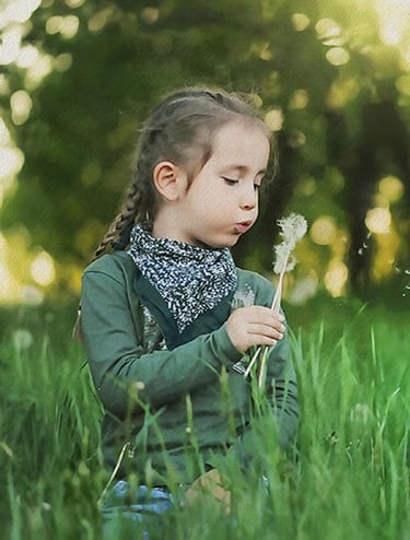 a little girl sitting in the grass with a dandelion