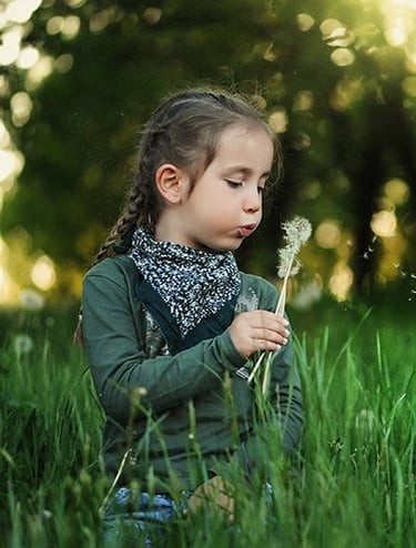 a little girl sitting in the grass with a dandelion
