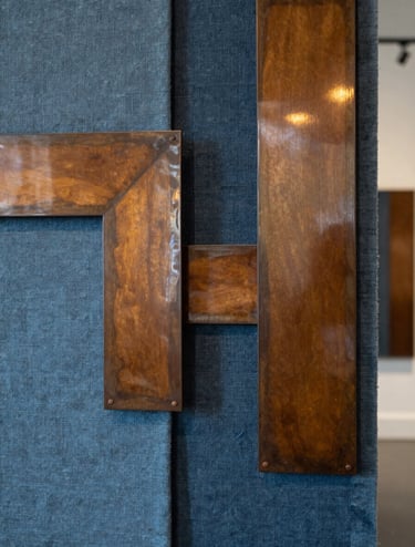 Photography of a mixed-media art installation in a Northern European / Welsh / British creative hub. The piece features raw Slate Blue textiles interwoven with polished Warm Ochre metal elements, reflecting a sophisticated and innovative approach to traditional craftsmanship in a contemporary setting.