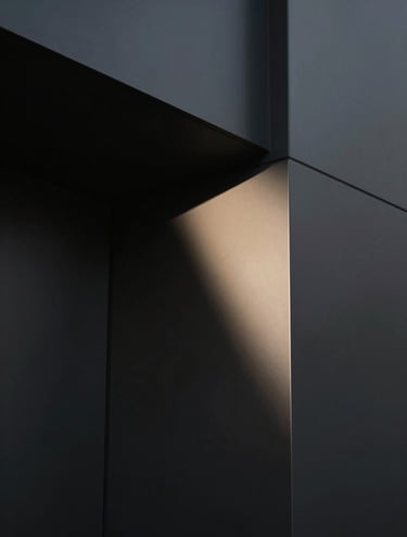 A sophisticated, minimalist architectural detail shot. Sharp geometric angles and deep shadows created by harsh lighting. The palette features deep blacks (#000000) and subtle sand-colored highlights (#B5A591) on a smooth surface. Clean, modern composition.