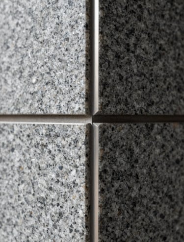 Macro detail shot of tectonic structural joints in the building. A combination of smooth granite gray surfaces and precise metal finishings, highlighting the studio's technical rigor and high-quality craftsmanship.