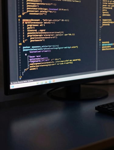 Close-up of a high-resolution digital screen in a dark room. The screen displays layers of code in a muted gold color, reflecting softly off a polished dark navy desk surface. The composition is clean and intellectual.