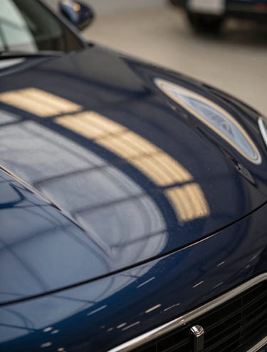 Close-up of a specialized PDR light board reflecting parallel gold and white lines on a car's curved body, showing the precision used to detect imperfections, professional lighting, navy blue car paint.