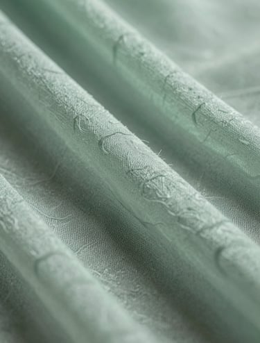 A macro close-up photograph of layered semi-transparent silk. The texture resembles a biological cell membrane. The colors are muted sage green and pale celadon. Soft, diffused lighting highlights the delicate weave.