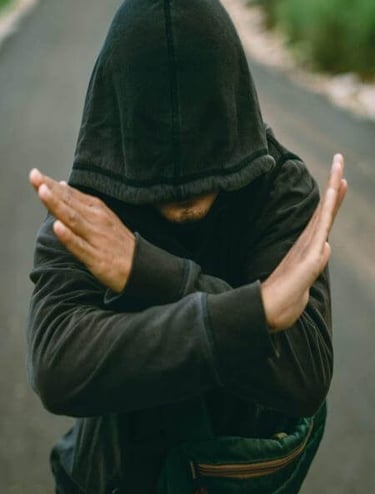Person in hooded sweatshirt standing on path with arms crossed in an “X” gesture.