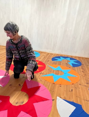 samuko arranging colorful star-patterned fabric circles on a wooden floor for a textile project.