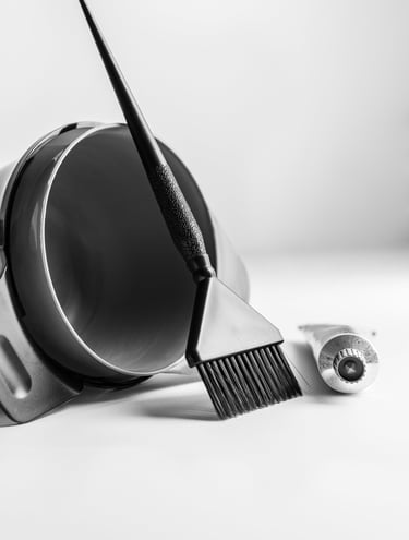 a black hair coloring bowl with brush leaning against it, hair color tube beside it