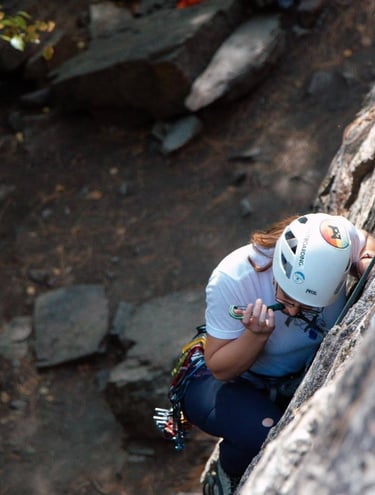 Person biting a cam while looking down and climbing a rock face. Photo credit: Brynn Weigelt.