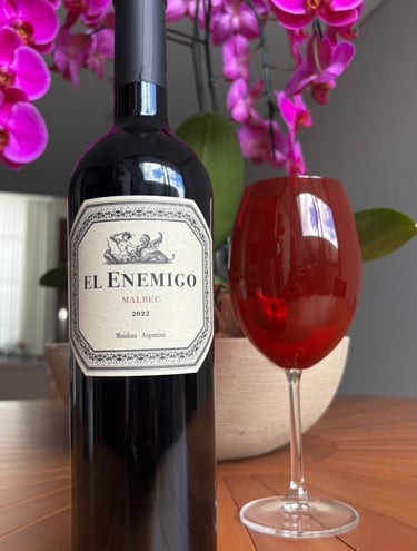 Garrafa de vinho El Enemigo Malbec 2022 ao lado de uma taça de vinho tinto decorada com orquídeas