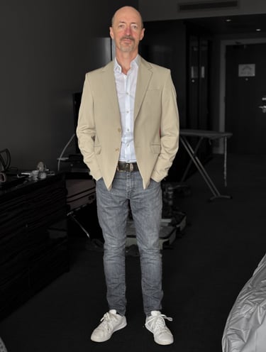 Portrait photo of Mark Murfitt wearing a cream colored jacked, white shirt, black jeans