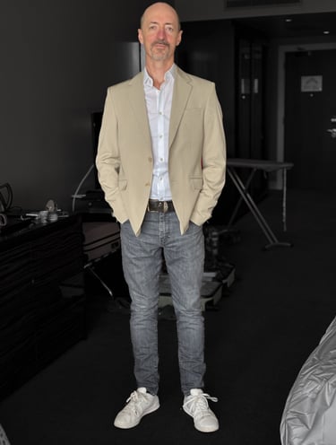 Portrait photo of Mark Murfitt wearing a cream colored jacked, white shirt, black jeans