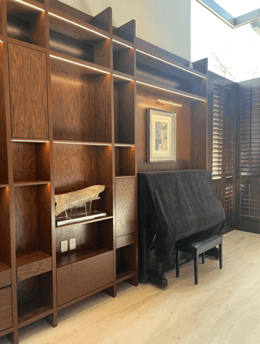 Estantería de madera iluminada con piano cubierto al fondo | KARÄNA
