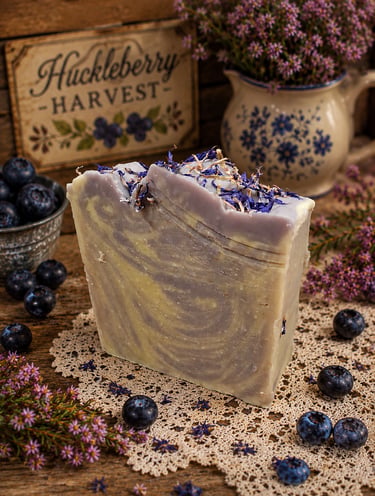 Handmade huckleberry swirl artisan soap bar topped with dried botanicals on a rustic wooden table.