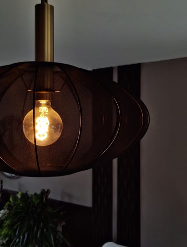 Un luminaire allumé en tissus noir devant un mur beige composé de panneaux décoratifs