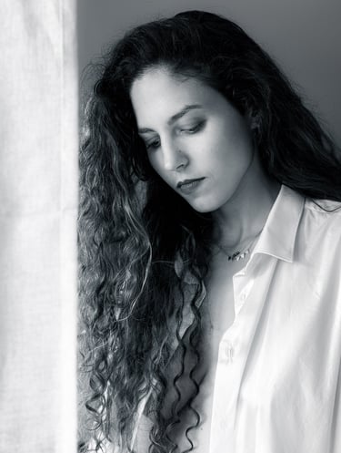 Black and white portrait of a woman with long curly hair, looking down under soft studio lighting.