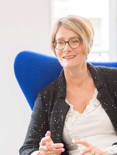 a woman in glasses and a black jacket sitting in a chair