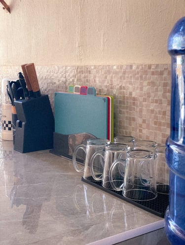 Kitchen countertop with glass mugs, colorful cutting boards, and a black knife block.