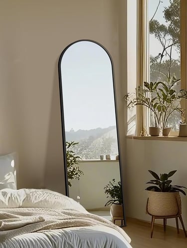 A full-length arched floor mirror with a black frame leaning against a wall in a bright, modern bedroom.