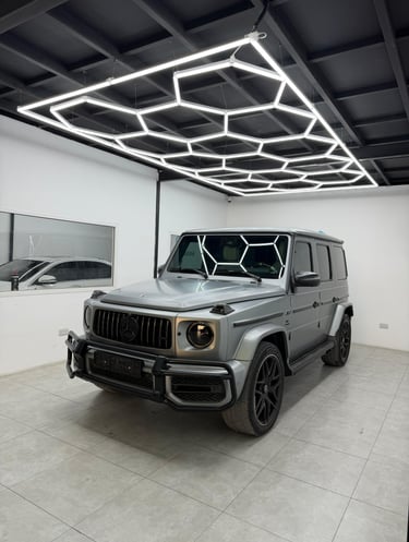 Silver Mercedes-Benz G-Class SUV parked in a garage with modern hexagonal LED ceiling lights.