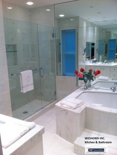 Modern luxury bathroom remodel featuring a glass walk-in shower, marble bathtub, and large vanity mirrors.