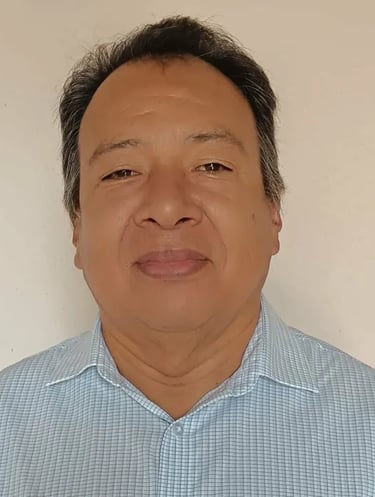 Professional headshot of a middle-aged man with short dark hair wearing a light blue checkered shirt.