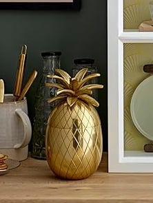 Gold pineapple ice bucket on a wooden shelf, decorative luxury home bar accessory.