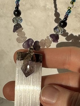 A crystal necklace with a shiny pendant made from selenite with an amethyst fixed on top