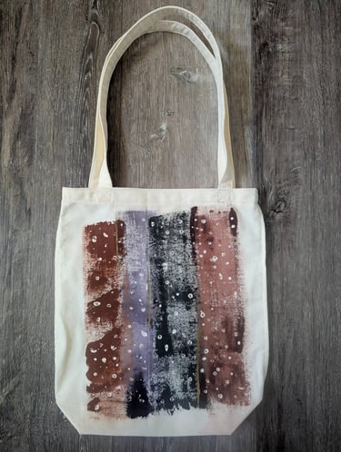 Hand-painted canvas tote bag with abstract plum and sage stripes, shown filled with groceries in a s