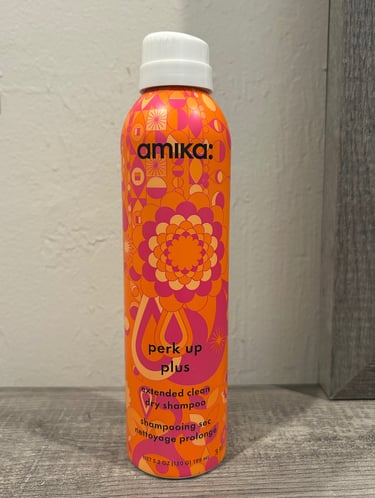 orange and pink Amika Perk Up Plus Dry Shampoo bottles on a bathroom counter