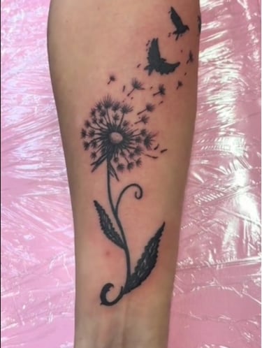 a tattoo of a dandelion flower on a woman's forearm