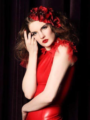 a woman in a red dress poses with a red flower in her brown curly hair