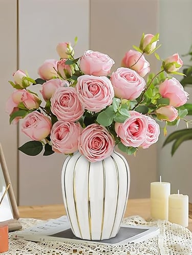 Gold and white ceramic vase filled with soft pink roses, modern luxury flower arrangement.
