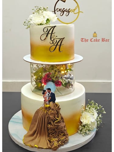 An elegant three-tier engagement cake featuring a gold ombré finish, custom initials, and a romantic